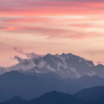 Montagne enneigée au coucher du soleil avec un ciel rose et nuageux.