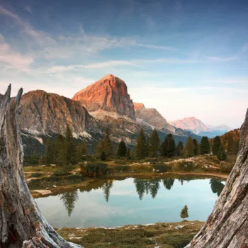 Paysage montagneux avec lac réfléchissant les pins entouré de formations rocheuses sous un ciel bleu clair
