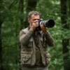 Photographe en tenue de terrain prenant des photos dans un environnement forestier