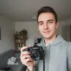 Un homme souriant tient un appareil photo dans un salon lumineux.