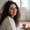 Femme souriante aux cheveux bouclés posant dans une pièce lumineuse avec des jouets en arrière-plan