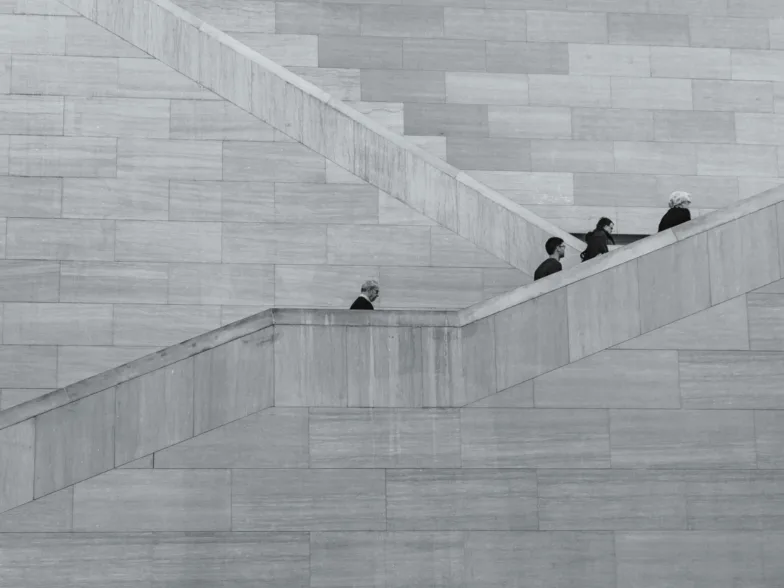 Des personnes montent un escalier en béton encadré par un mur en briques grises.