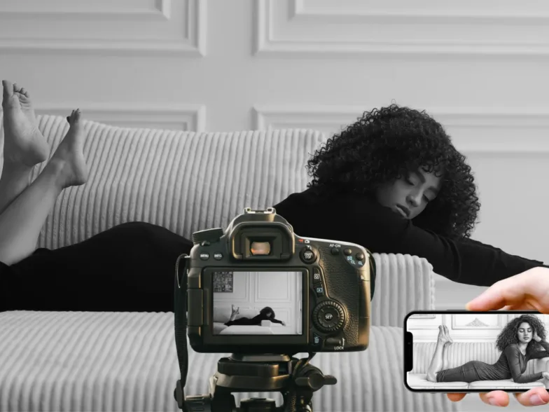 Une femme allongée sur un canapé est photographiée en noir et blanc avec un appareil photo et un smartphone.